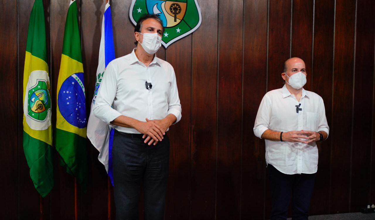governador e prefeito lado a lado de máscara, posando para a câmera e com bandeiras ao fundo